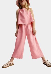 Ensemble rose en deux pièces comprenant un top sans manches avec des bords festonnés et un pantalon à jambes larges. Tissu léger avec une coupe décontractée.