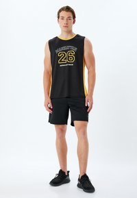 Svart ärmlös sportskjorta med gul kant, med texten "MANHATTAN 26 RECREATION CENTER." Matchat med svarta shorts och svarta sneakers.