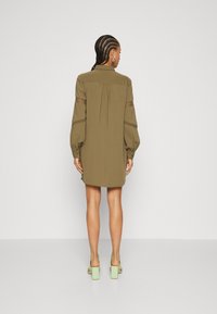 Olive green shirt dress with long puffed sleeves and side slits. It features a button-up design and mesh detailing on the sleeves.