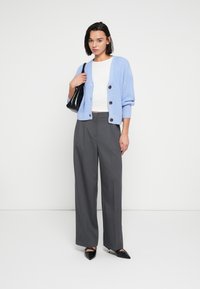 Ανοιχτό μπλε πουλόβερ με μεγάλα καφέ κουμπιά, λευκό εφαρμοστό τοπ, γκρι φαρδιά παντελόνια και μαύρες γόβες με μυτερή μύτη. Μαύρη τσάντα χειρός.