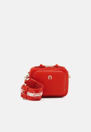 Bolso pequeño rojo de cuero para llevar cruzado, con bolsillo frontal, logo dorado y correa ancha ajustable de tela con diseño blanco y rojo.