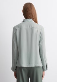 Light green, smooth satin shirt with a collar, buttoned cuffs, and a straight back design. Minimalist style and structured cut.