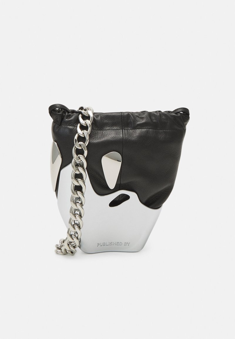 Borsa a secchiello in pelle nera con una base argentata lucida, dotata di una tracolla oversized in catena e dettagli intagliati. Parte superiore strutturata, chiusura con cordoncino.