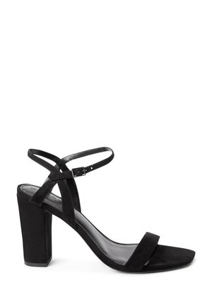 Black suede high-heeled sandal with a block heel, open toe, ankle strap, and small buckle, shown in side profile on a white background.