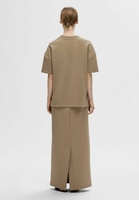 Beige todelt outfit bestående af en kortærmet top i boxy stil og en lang nederdel med en slids bagpå, lavet af et glat, blødt stof.
