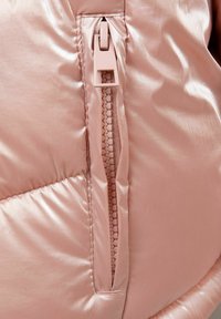 Giacca a vento rosa in tessuto con finitura lucida, dotata di chiusura con zip laterale e dettagli trapuntati per isolamento e stile.