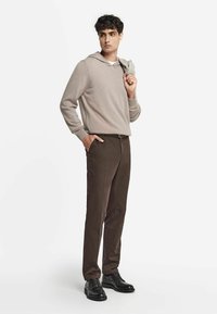 Hellebeige Kapuzenpullover, braune maßgeschneiderte Hosen und schwarze Schnürschuhe. Glatter Stoff, lockere Passform und subtile Details.
