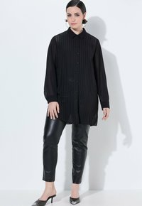 Zwarte doorschijnende button-up shirt met verticale strepen, lange mouwen en een kraag, gecombineerd met zwarte strakke faux leren broek en hoge hakken.