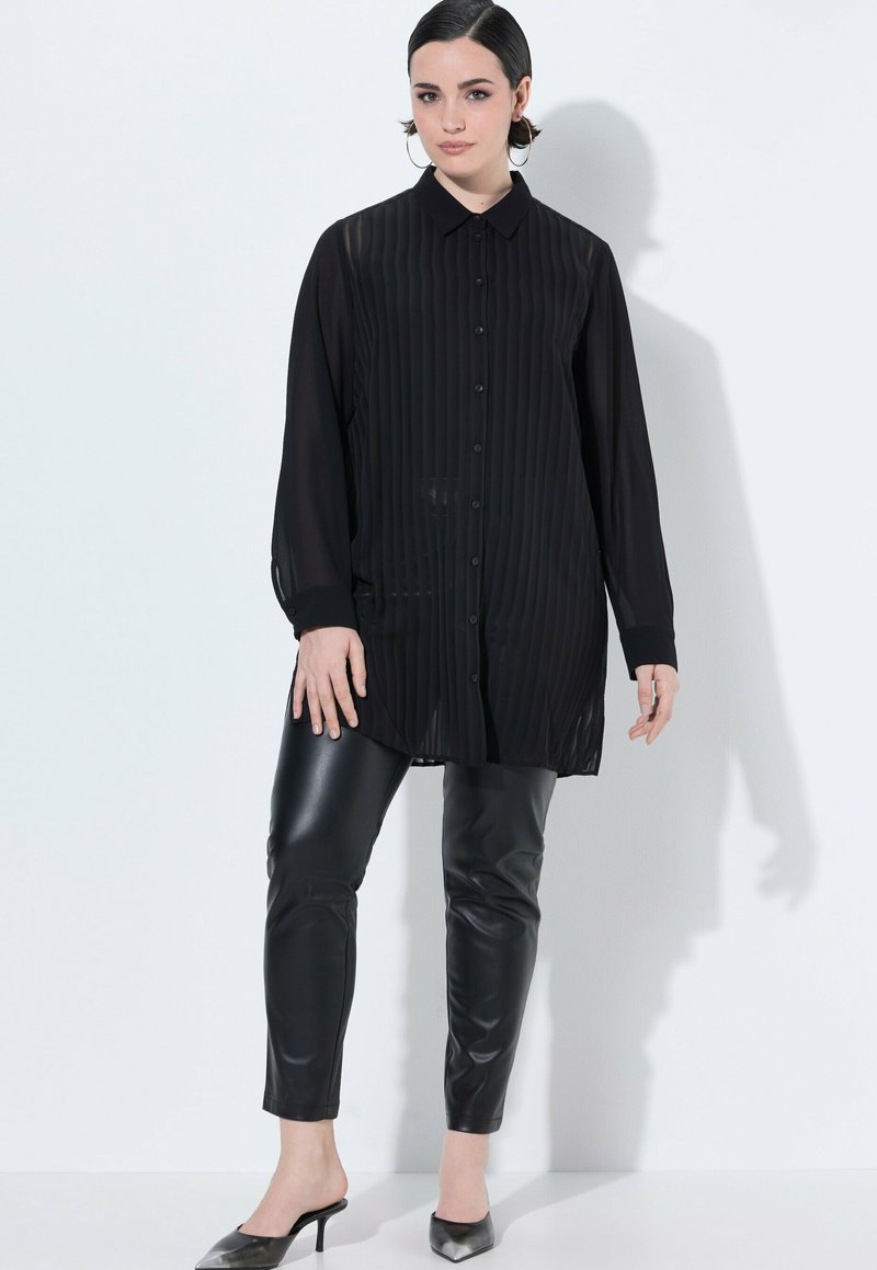 Zwarte doorschijnende button-up shirt met verticale strepen, lange mouwen en een kraag, gecombineerd met zwarte strakke faux leren broek en hoge hakken.