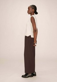 Un haut en tricot sans manches de couleur gris clair associé à un pantalon large taille haute de couleur marron foncé et des mocassins en cuir noir.