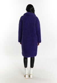 Palton mov, pufoș, cu guler, până la genunchi, cu o croială supradimensionată. Puratat peste leggings negri, lucioși și cizme albe cu toc pătrat. Design simplu.