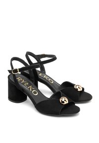 Czarne zamszowe sandały na obcasie z krzyżującymi się paskami, regulowanym paskiem na kostce i okrągłym złotym akcentem z przodu. Gruby blokowy obcas.