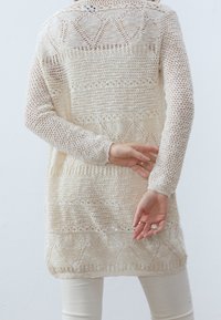 Pletený kardigan v krémové barvě s dlouhými rukávy, s texturovaným háčkovaným vzorem a geometrickými akcenty. Styl s otevřeným zády, lehký materiál.