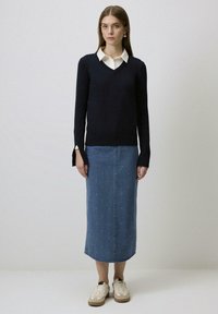 Marineblauwe V-halstrui met lange mouwen, gecombineerd met een middellange spijkerrok in het blauw met kleine witte parels, en witte sneakers.