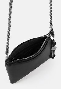 Bolso de mano negro de cuero con una correa de cadena, cierre de cremallera y textura suave. El interior presenta un forro de tela y una pequeña etiqueta con la marca.