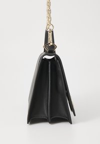 Czarna skórzana torebka o wyrazistym kształcie, z złotym łańcuszkiem i płaskim, podzielonym wnętrzem. Gładka tekstura.