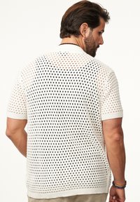 Weißer kurzärmeliger Strickpullover mit offenen Löchern, der ein strukturiertes Muster und gerippte Bündchen aufweist. Von hinten angezeigt.