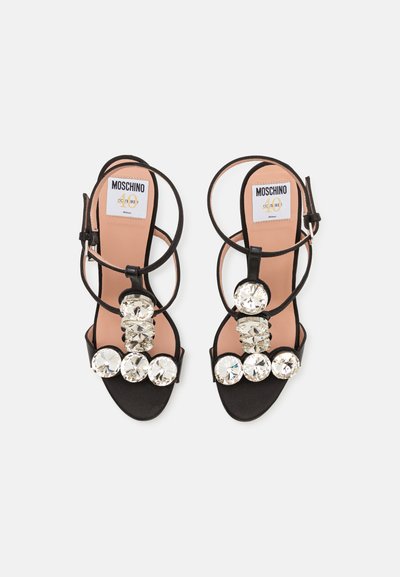 Melnas augstpapēžu sandales ar vairākām lielām caurspīdīgām rhinestones priekšējā siksniņā, regulējama potītes siksna un gluda ķermeņa krāsas iekšējā zole.