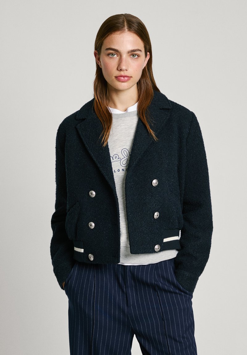 Marineblaue, taillierte, doppelt-knöpfbare Jacke aus strukturiertem Stoff mit silbernen Knöpfen, Fronttaschen und weißen Streifenakzenten am Saum.