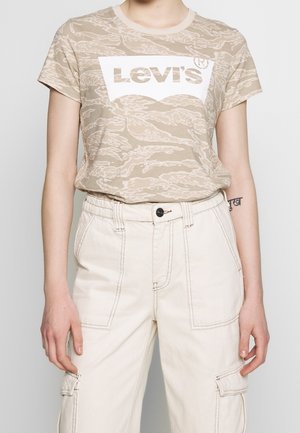 Personne portant un t-shirt Levi's beige camouflage, rentré dans un pantalon cargo taille haute blanc cassé avec des poches à rabat et à boutons.