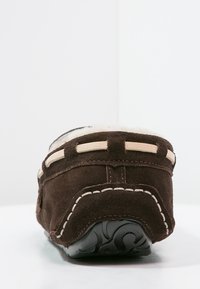 Scarpa slip-on in suede marrone con una morbida fodera in pelliccia e cuciture beige a contrasto. Presenta una suola in gomma nera testurizzata.