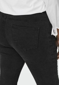 Black denim jeans featuring a classic design with a single back pocket and a smooth texture. The fabric appears slightly worn at the edges.