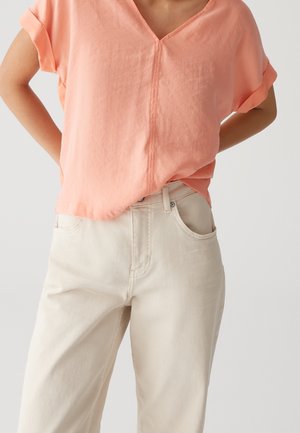 Person wearing loose peach V-neck short-sleeve top tucked into high-waisted off-white wide-leg pants against plain background.