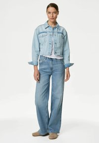 Giacca di denim azzurro chiaro e jeans a gamba larga indossati sopra una t-shirt bianca. La giacca ha tasche e un design corto. Tessuto morbido e strutturato.