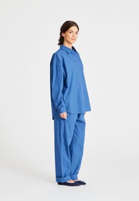 Cămașă albastră, cu croială lejeră, cu butoni și pantaloni asortați dintr-un material ușor, având un design relaxat și mâneci lungi.