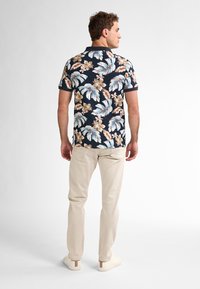 Polo de manga corta con fondo navy, que presenta un patrón floral en azul claro, marrón y crema. Combinado con pantalones beige claros.
