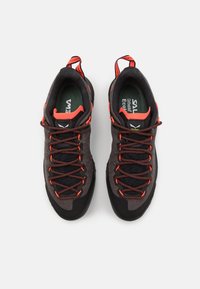 Musta ja harmaa vaelluskengät, joissa on punaisia yksityiskohtia, teksturoitua kangasta ja kestäviä kumipohjia. Nyörit ovat mustat punaisilla pilkuilla.