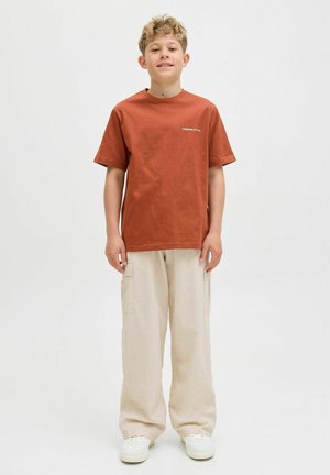 Krótki rękaw, rdzawoczerwony t-shirt z bawełny z haftowanym detalem, zestawiony z jasnobeżowymi spodniami cargo i białymi trampkami, stojący na jednolitym tle.