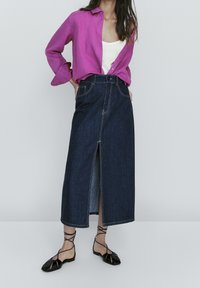 Dark blue denim skirt with a front slit, accented by yellow stitching. Paired with a bright pink button-up shirt and black strappy flats.