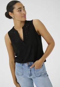 Haut sans manches noir avec un design en œillets texturé, arborant un décolleté en V et une coupe ample, associé à un jean taille haute bleu clair.