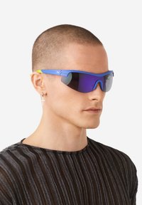 Plave sunčane naočale sa žutim detaljima, omotnim dizajnom, reflektirajućim ljubičastim lećama i teksturiranim okvirom. Minimalistički oblik i sportski stil.