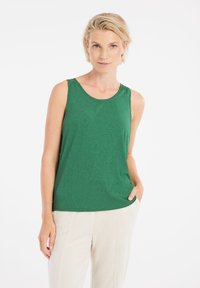 Top in tessuto texturizzato verde senza maniche, con scollatura a barchetta e vestibilità comoda, abbinato a pantaloni di colore chiaro.
