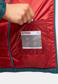 Czerwona, ocieplana kurtka z szarym metki wewnątrz. Na metce widnieją informacje o właściwościach wodoodpornych i izolacyjnych, a także ręka sięgająca do kieszeni.