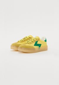 Gule semsket sneakers med grønn lynbolt-design, har teksturert overdel, rund tå, gule lisser og gjennomsiktig gummisåle.