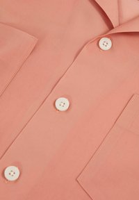 Ljus korallfärgad button-up skjorta i mjukt tyg, med en liten ficka och vita knappar, samt en enkel vikkrage.