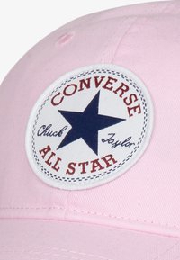 Rosa baseball cap med et rundt brodert merke med en marinebl�å stjerne, rød tekst som sier "Converse All Star," og syedetaljer.