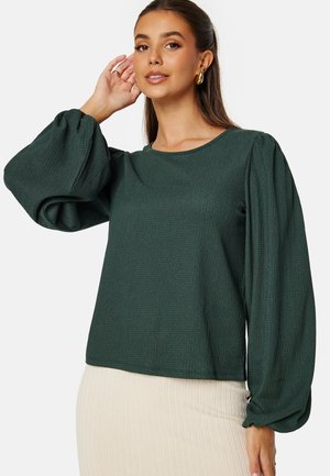 Dark green, textured long-sleeve top with puffed sleeves and a round neckline, paired with a light ribbed skirt. Elegant and fitted design.