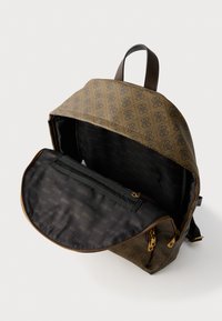 Mochila marrón con estampado, asa de cuero y bolsillo frontal abierto que muestra el forro de tela negra con estampados de logotipos "GUESS".