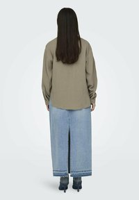 Olijfgroen shirt met lange mouwen, gecombineerd met een lichtblauwe spijkerrok met een achternek en donkerblauwe schoenen. Gladde stoftextuur zichtbaar.