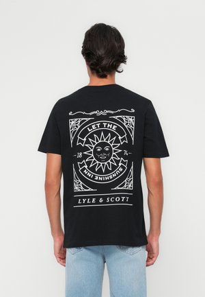 T-shirt en coton noir avec un grand graphisme blanc au dos, incluant un design de soleil, du texte et des bordures détaillées. Col rond, manches courtes.