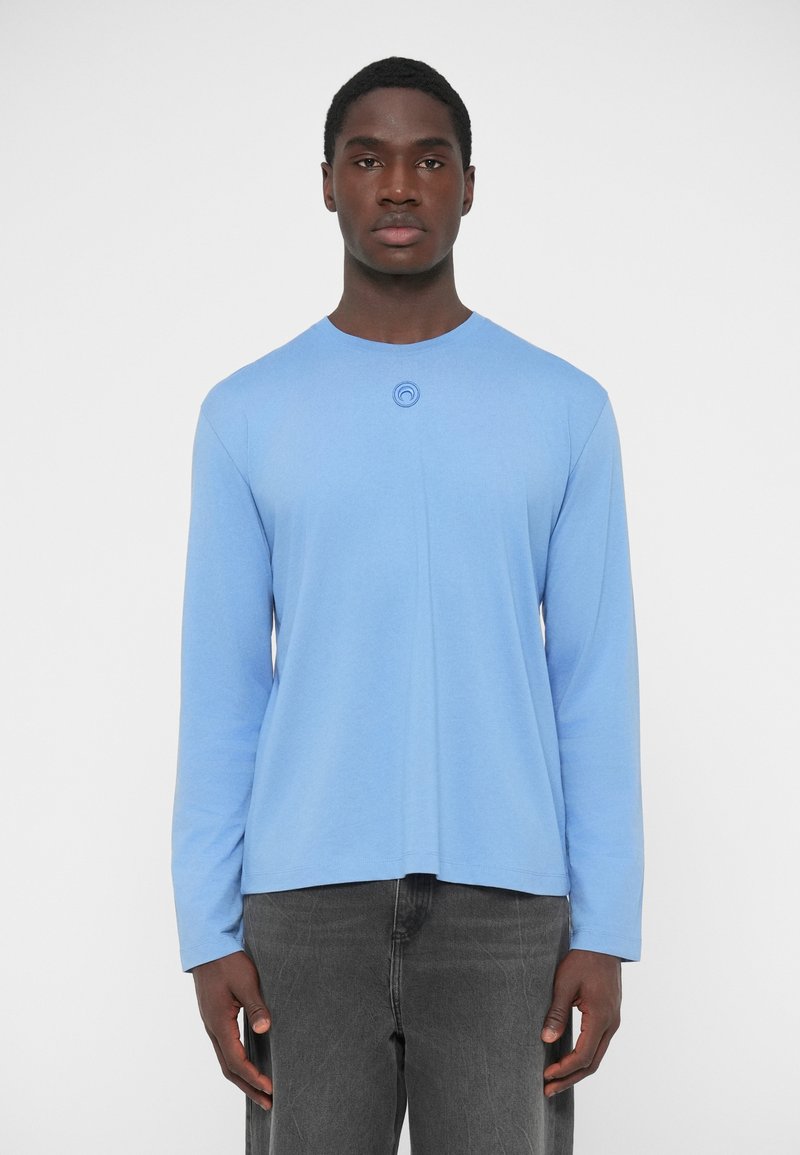 Svetlomodré tričko s dlhými rukávmi vyrobené z bavlny, s okrúhlym výstrihom a kruhovým logom na hrudi, kombinované so sivými nohavicami.