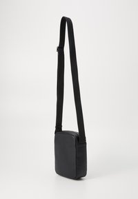 Schwarze, strukturierte Umhängetasche mit quadratischer Form und verstellbarem Nylonriemen. Verfügt über einen Reißverschluss und ein minimalistisches Design.