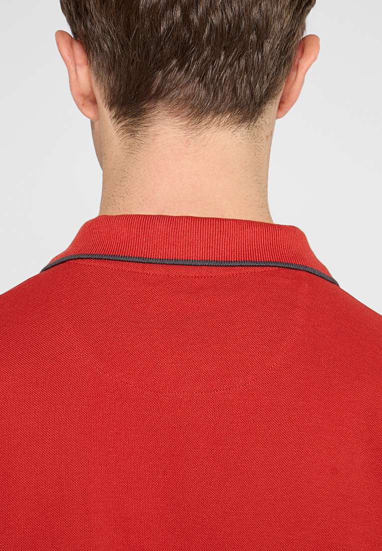 Camisa polo roja con tejido texturizado, cuello con un ribete oscuro en contraste y un diseño trasero limpio.