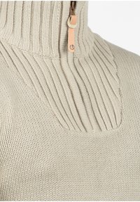 Beige gebreide trui met een hoge geribbelde kraag en een rits, voorzien van een leren trekker en een textuurpatroon op het nekgebied.