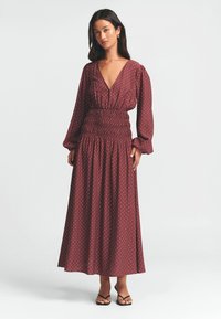 Mekko on viininpunainen pitkähihainen, syvällä V-päällä, smokkihyytelöidyllä vyötäröllä ja valkoisilla palloilla. A-linjainen malli pehmeästä kankaasta, jossa on hienovarainen tekstuuri.