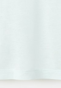 Gros plan sur un tissu blanc uni avec des coutures visibles et une texture au niveau de l'ourlet d'un vêtement.